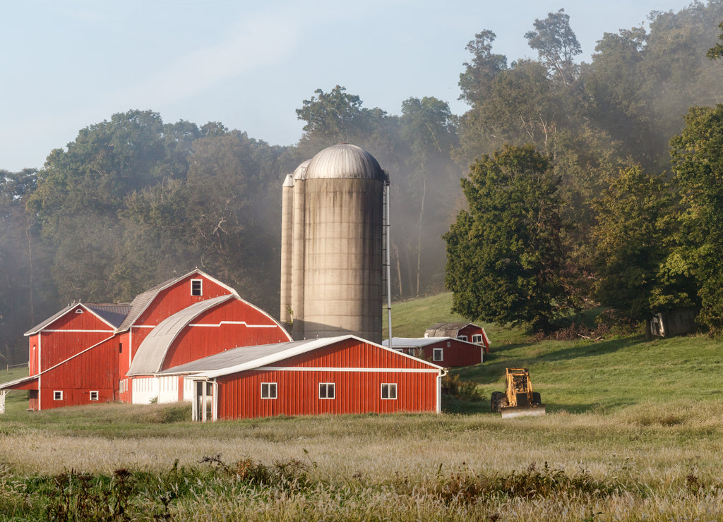 Red barns with a silo beside the woods on an Amish farm in Holmes County, Ohio