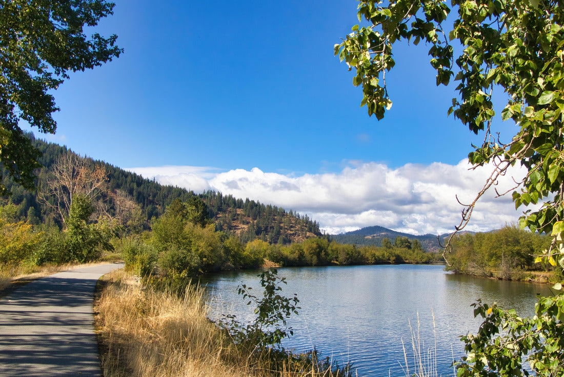 On a sunny fall day in North Idaho, the path of the Coeur d'Alenes runs between a peaceful river and forested hills, with clouds and mountains in the distance 2000pc Puzzle