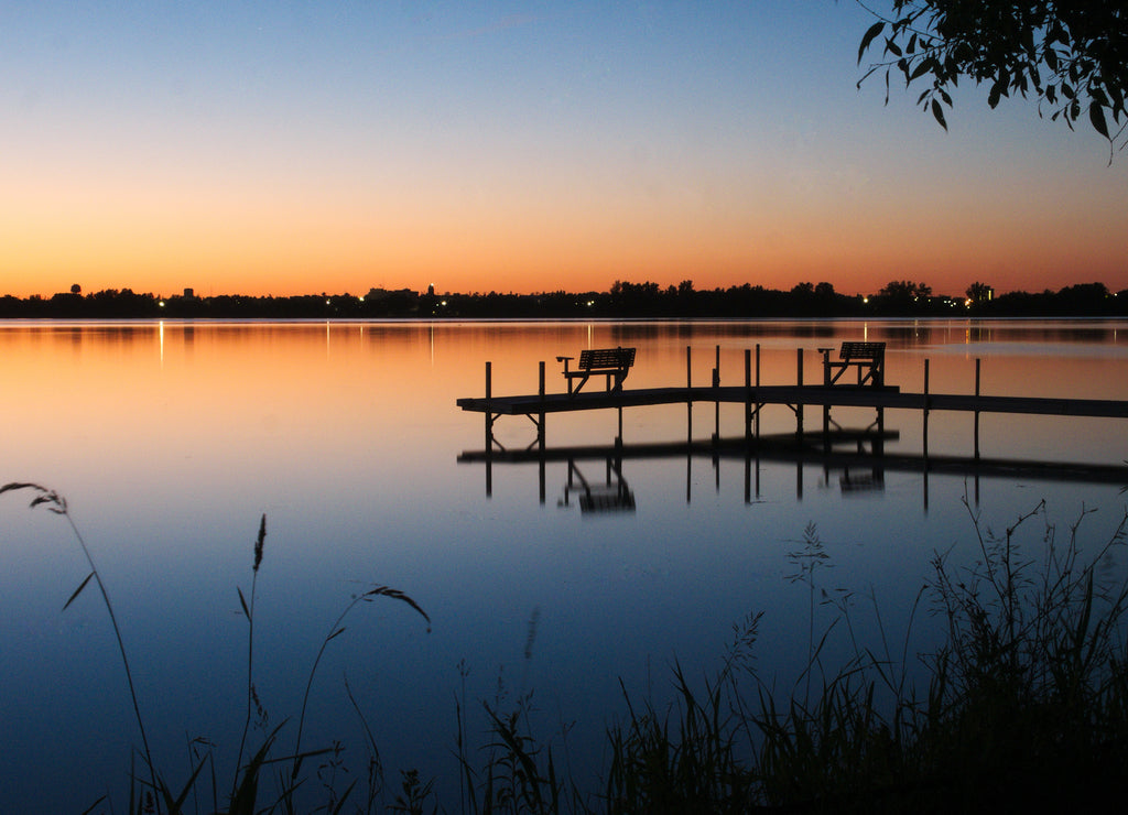 Bemidji, Minnesota, the Best Town in Minnesota is seen across Lake Irving, the first lake on the Mississippi River, after sunset in summertime. A dock is seen in the foreground in this night photo