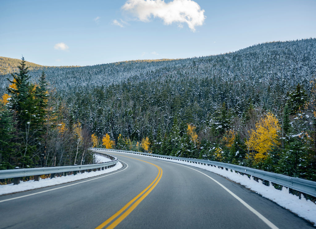 Winding highway between wooded mountains with evergreen and deciduous trees sprinkled with the first snow on a pass in Vermont