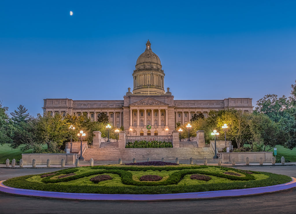 Kentucky State Capitol at dusk with warm lights illuminating this great capitol with a blue sky with a half moon on a warm summer evening in Frankfort, KY