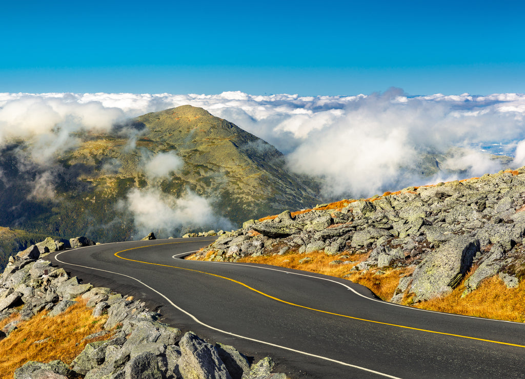 Winding road descending from Mount Washington, New Hampshire on a sunny autumn afternoon. Mount Jefferson peak stands above a thick layer of fluffy clouds