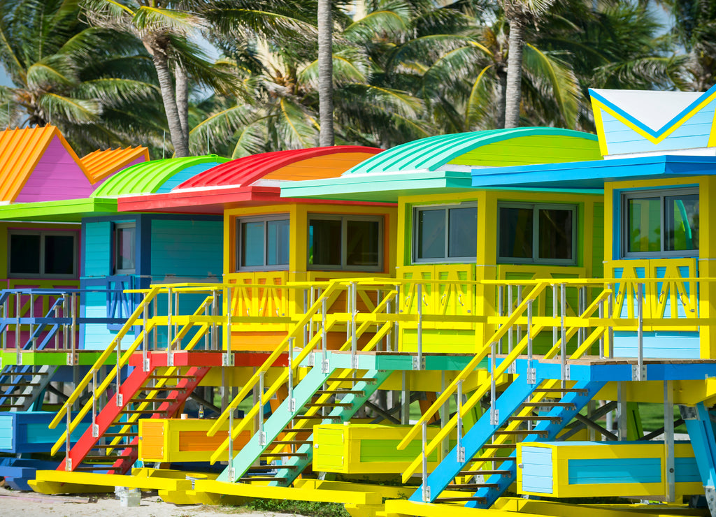 Colorful scenic morning view of brightly painted lifeguard towers with coconut palm trees on the South Beach promenade in Miami, Florida, USA