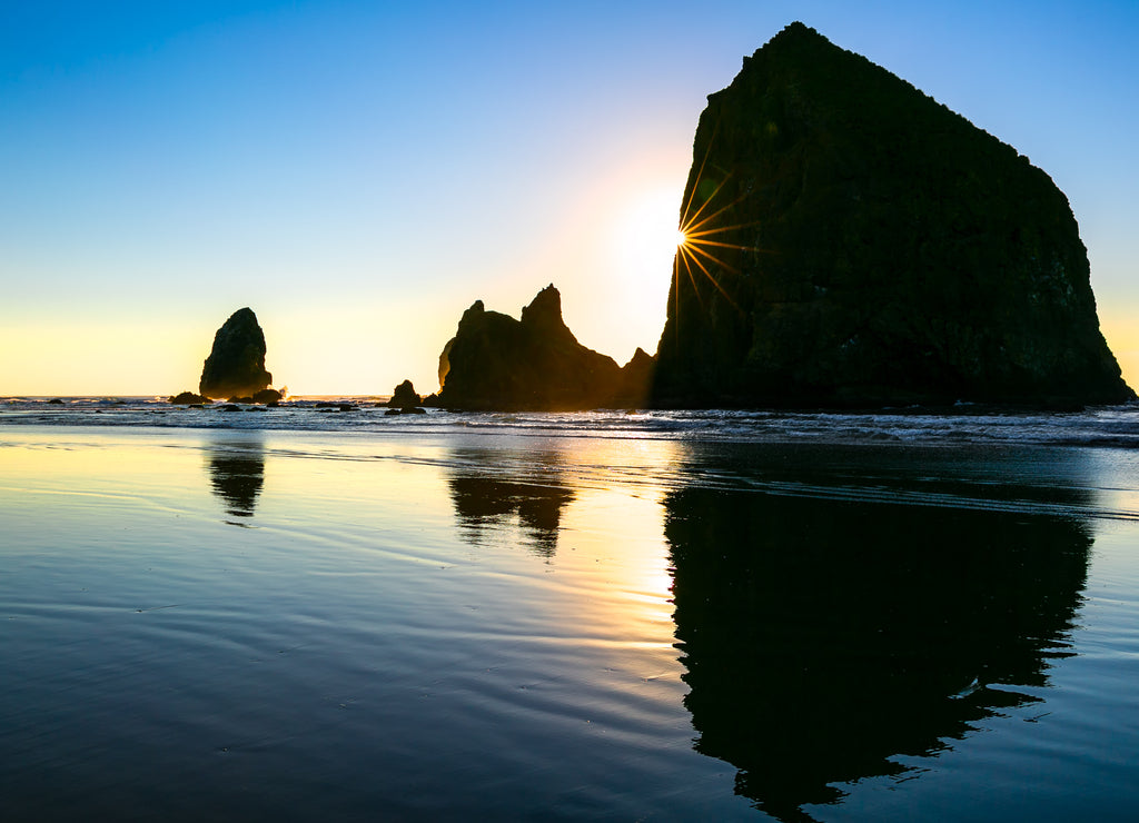 Silhouette of famous sea stack rock formations with natural sun flare. Cannon Beach, Oregon USA
