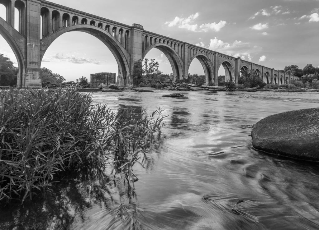 Richmond Railroad Bridge Lit by Sun/ The graceful arches of a railroad bridge spanning the James River in Virginia are illuminated by the setting sun in black white