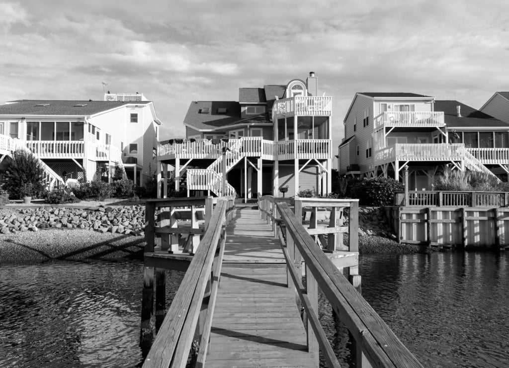 Long wooden dock leading to three luxury vacation rental beach houses on the intercoastal waterway, Sunset Beach, North Carolina in black white